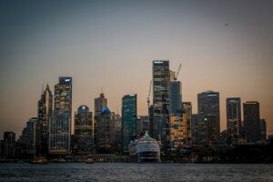 Modern cityscape with skyscrapers and a cruise ship at dusk.